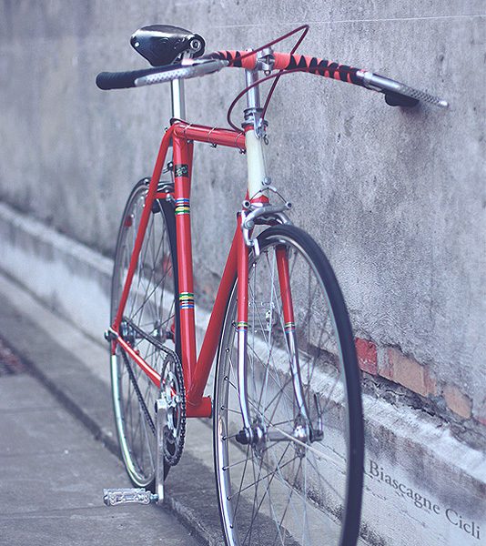 Red steel road bike leaning against a concrete wall