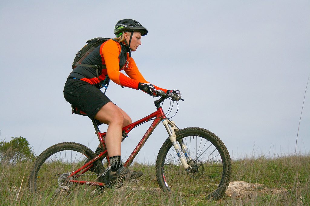 Mountain biker in orange riding across a grassy hill